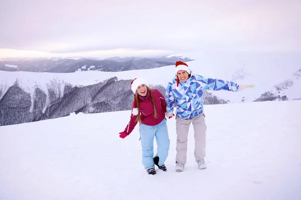 Casal feliz em chapéus de Papai Noel se divertindo no resort nevado. Férias inverno — Fotografia de Stock