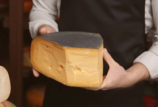 Jonge werknemer houdt stuk kaas in winkel — Stockfoto