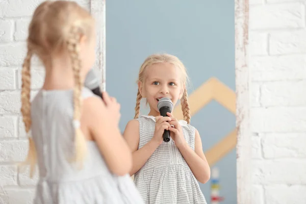 Schattig klein meisje met microfoon poseren voor de spiegel binnenshuis — Stockfoto