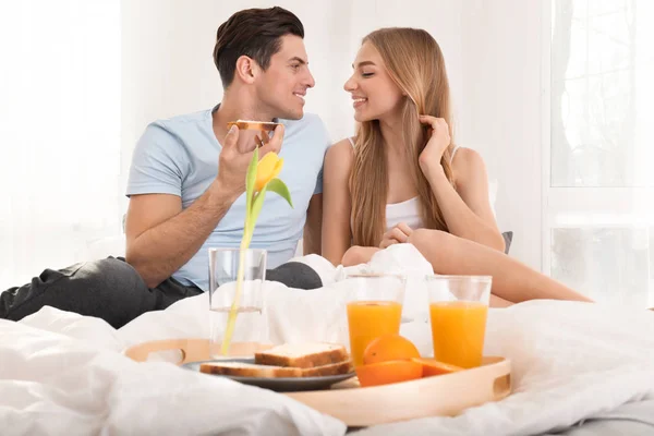 ベッドで朝食を持っている若い素敵なカップル — ストック写真