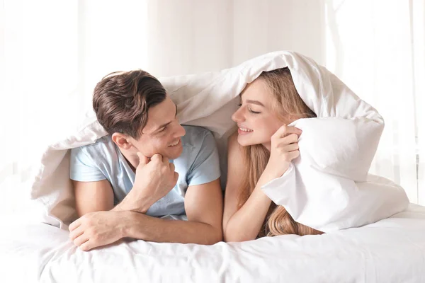 Young couple under blanket in bed at home