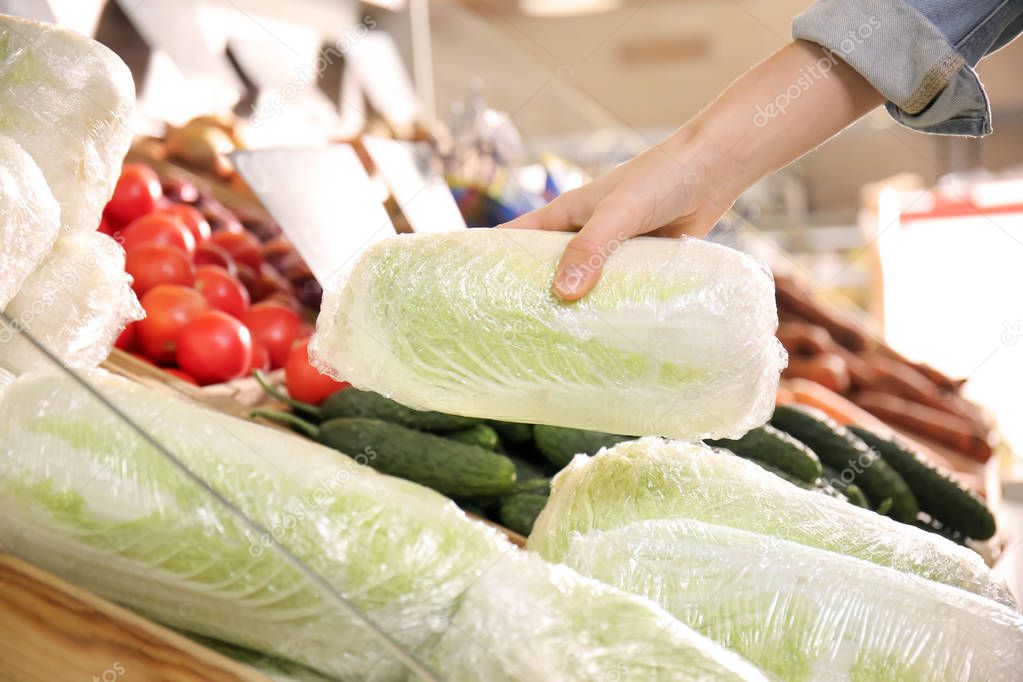 Young woman choosing fresh napa cabbage in supermarket