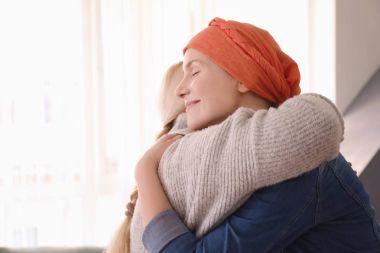 Young woman with cancer hugging her mother indoors clipart