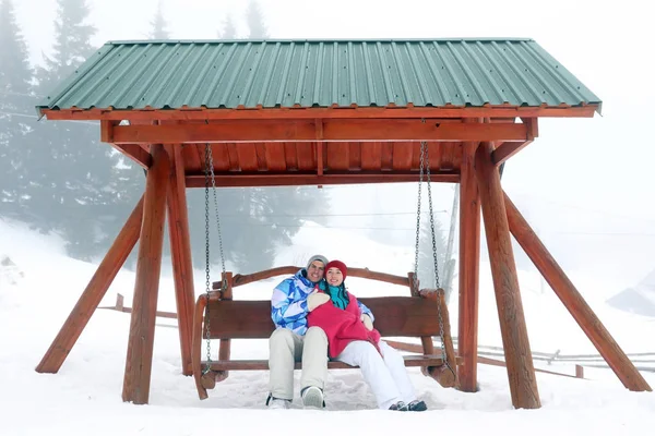 Casal encantador no banco balançando no resort nevado. Férias inverno — Fotografia de Stock