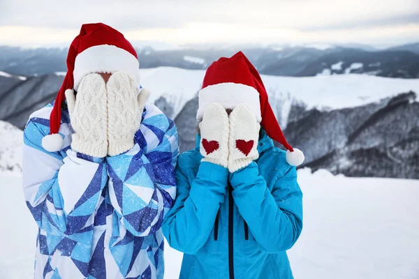 Joyeux couple dans des chapeaux de Père Noël et des mitaines chaudes s'amusant à la station enneigée. Vacances d'hiver — Photo