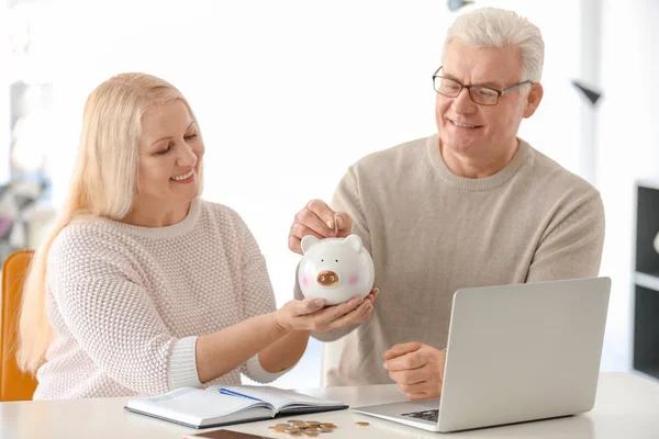 Mature Couple Putting Coin Piggy Bank Home — Stock Photo, Image