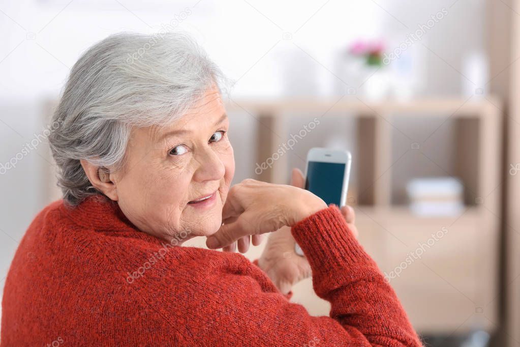 Mature woman with hearing aid using smartphone indoors