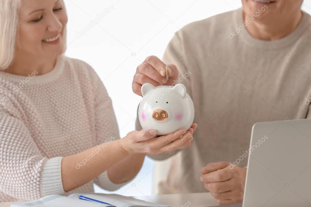 Mature couple putting coin into piggy bank at home