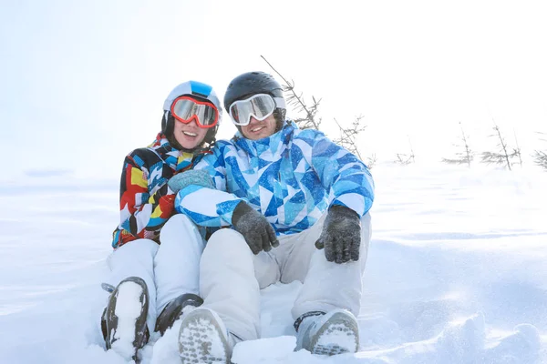 Casal feliz sentado na neve na estação de esqui. Férias inverno — Fotografia de Stock