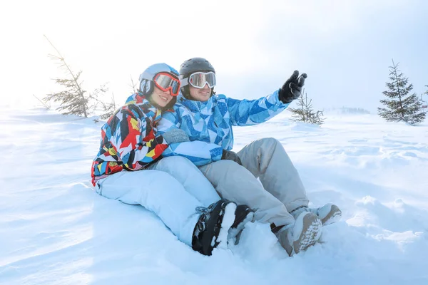 Casal feliz sentado na neve na estação de esqui. Férias inverno — Fotografia de Stock