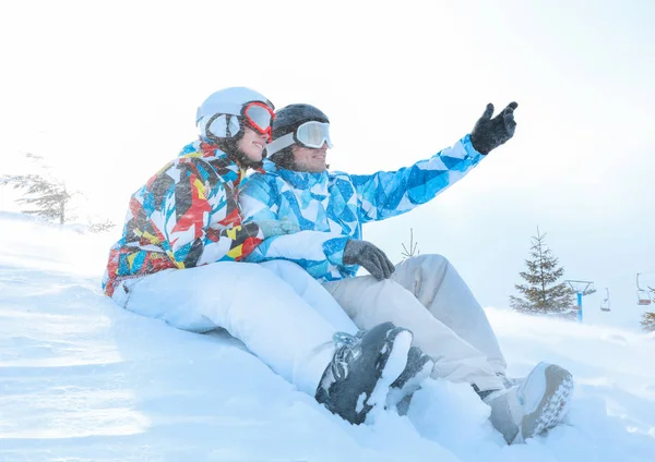 Casal feliz sentado na neve na estação de esqui. Férias inverno — Fotografia de Stock