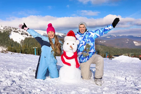 Joyeux couple avec bonhomme de neige à la station de ski. Vacances d'hiver — Photo