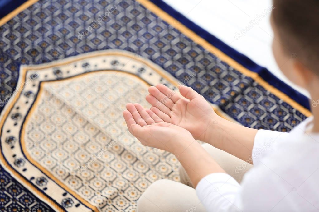 Young Muslim man praying on rug, closeup