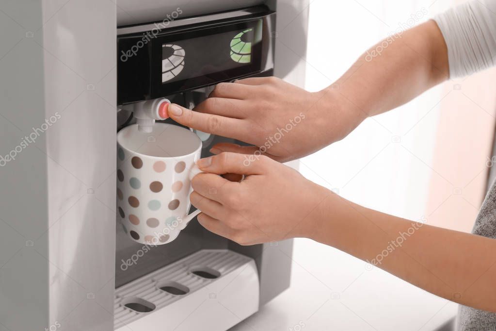 Woman filling cup from water cooler, closeup