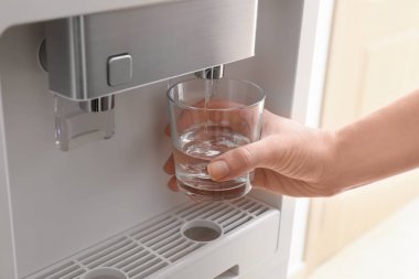 Woman filling glass from water cooler, closeup clipart
