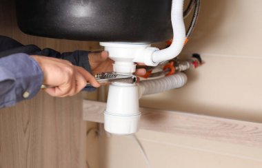Professional male plumber replacing sink trap indoors clipart