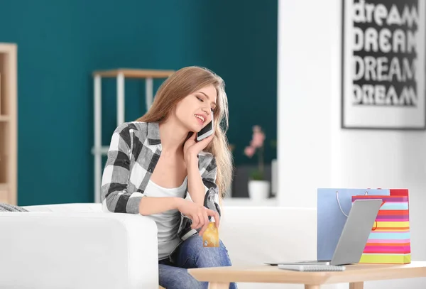 Jovem com laptop e cartão de crédito conversando no telefone no quarto. Compras online — Fotografia de Stock