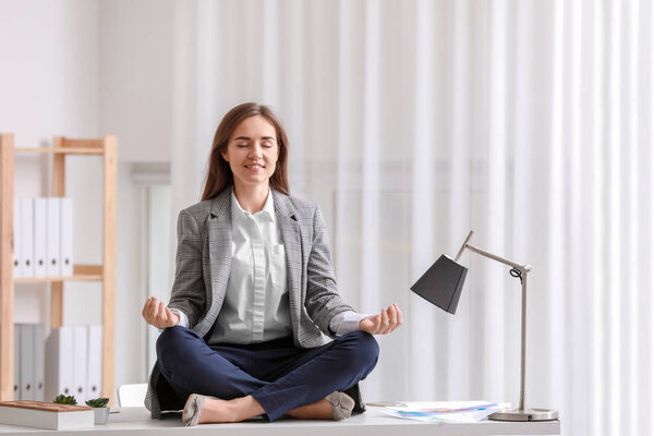 Young woman meditating on table in office