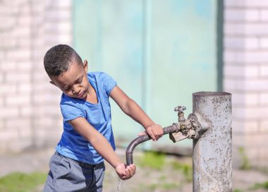 African American child drinking water from tap outdoors. Water scarcity concept clipart