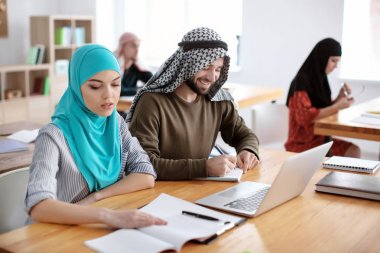 Erkek öğrenci ve onun Müslüman sınıf kitaplığında dizüstü bilgisayar kullanarak