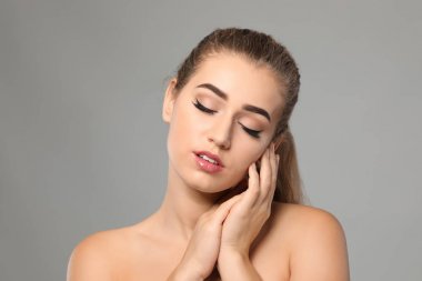 Gri arka planda güzel kaşları olan genç bir kadın.