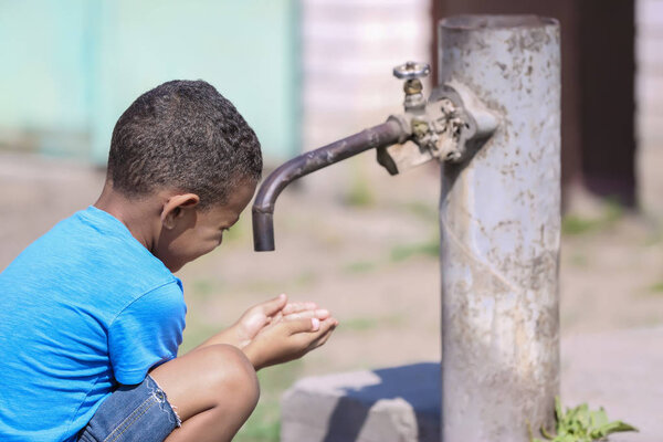 Cute African American boy sitting near tap, outdoors