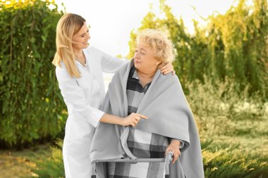 Senior woman with walkers and nurse from care home in park clipart
