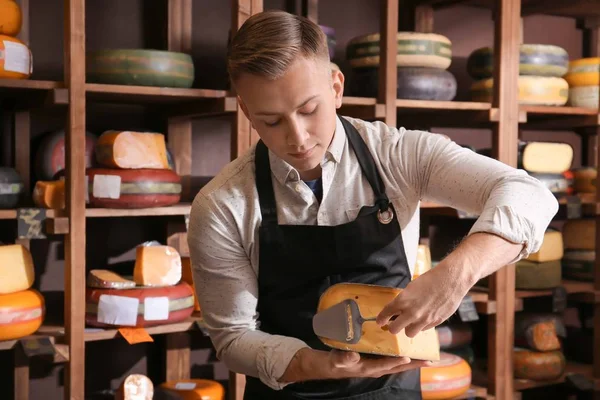 Young worker slicing cheese in shop