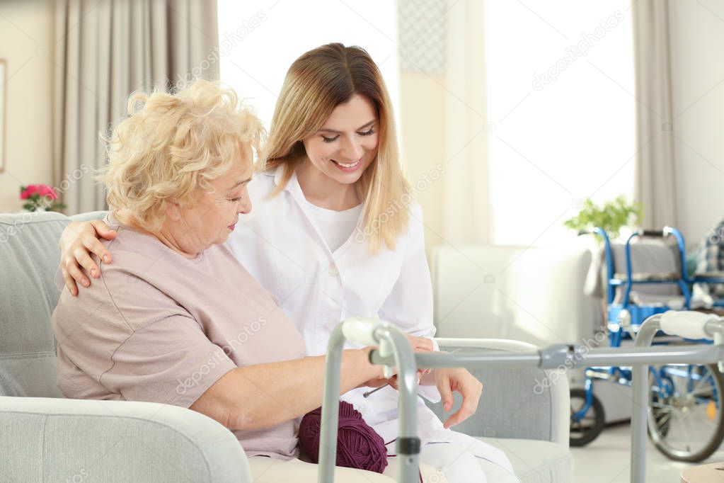 Senior woman sitting on sofa and knitting while talking with nurse at care home