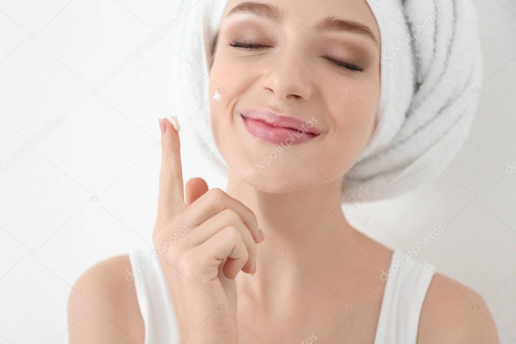 Young woman applying face cream, on white background