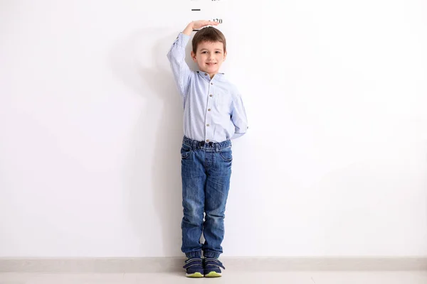 Height of child grow up. Little boy measuring his height on white