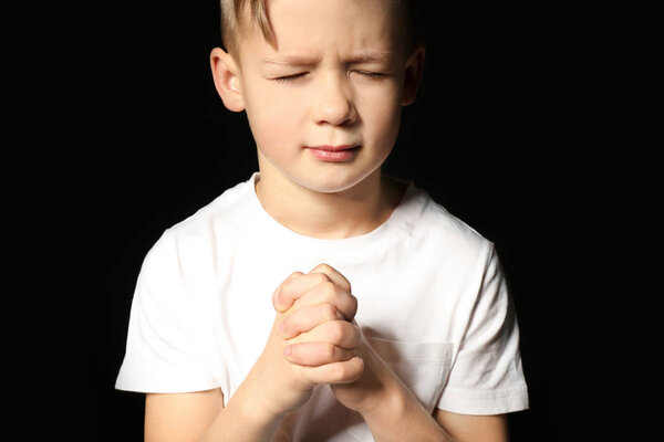 Religious little boy praying on black background