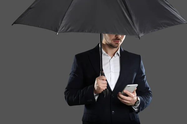 Junger Mann Mit Regenschirm Und Smartphone Auf Grauem Hintergrund — Stockfoto