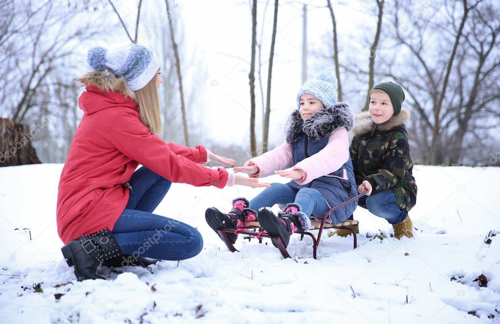 Happy mother with children sledding in snowy park on winter vacation