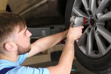 Mechanic changing car wheel in garage. Tire service clipart