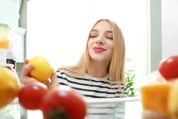 Молодая женщина со свежим лимоном рядом с открытым холодильником, вид изнутри — стоковое фото
