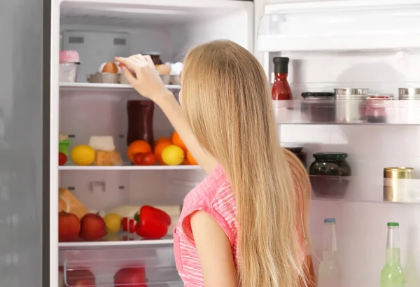 Young woman near open refrigerator in kitchen