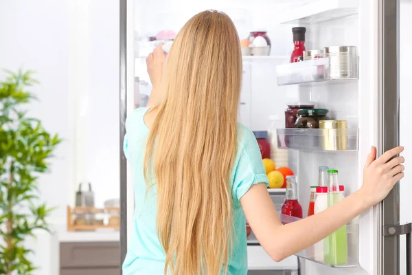 Ung kvinna nära öppna kylskåpet i köket — Stockfoto