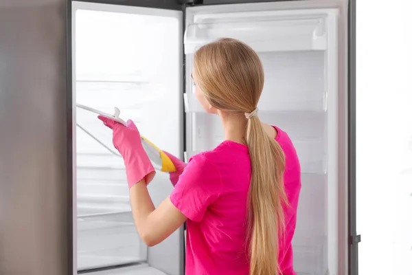 Woman cleaning refrigerator in kitchen