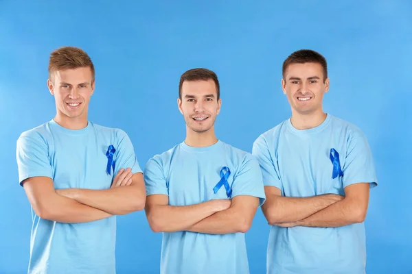 Young men in t-shirts with blue ribbons on color background. Prostate cancer awareness concept