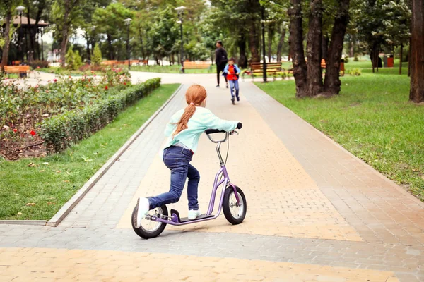 Mignonne petite fille équitation kick scooter dans le parc — Photo