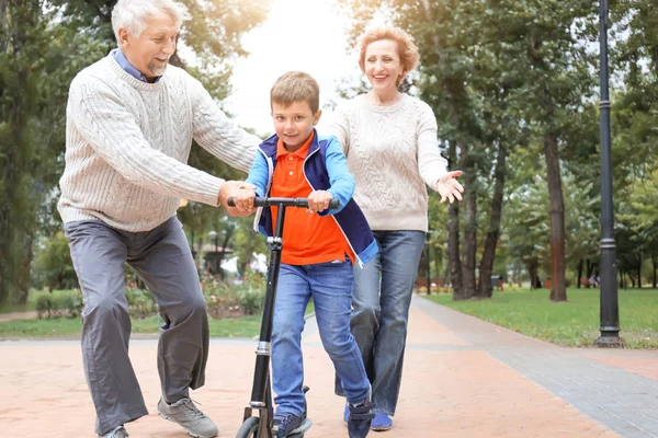 Glückliches Seniorenpaar mit Enkelkind fährt Tretroller im Park — Stockfoto