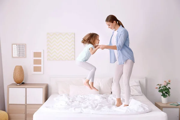 Happy mother and her daughter jumping on bed in children room