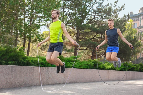 Unga män i sportkläder med hoppning rep i park — Stockfoto