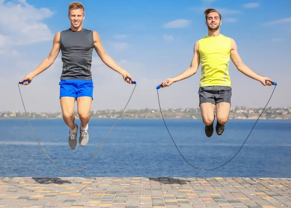 Young men in sportswear with jumping ropes on quay — Stock Photo, Image