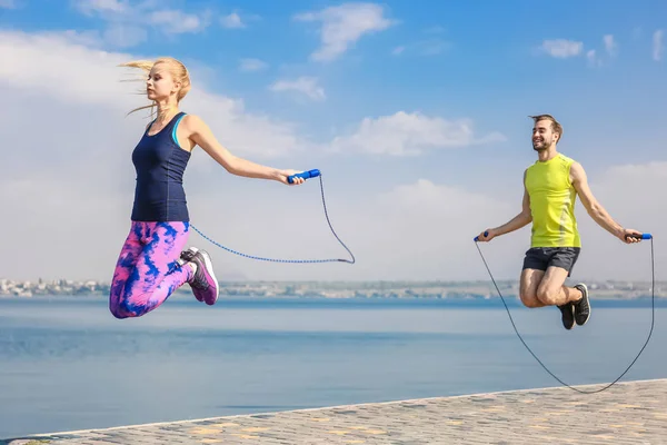 Young man and woman with jumping ropes on quay