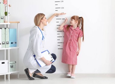 Female doctor measuring height of little girl in clinic clipart