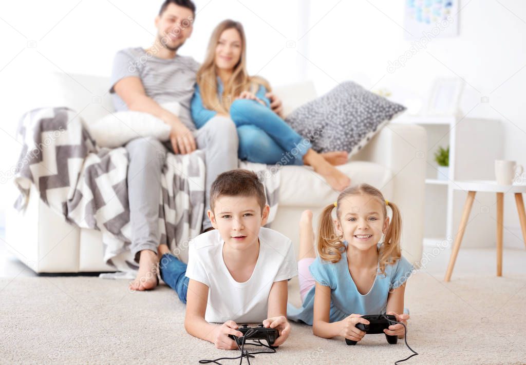 Cute children playing video games while parents resting on background