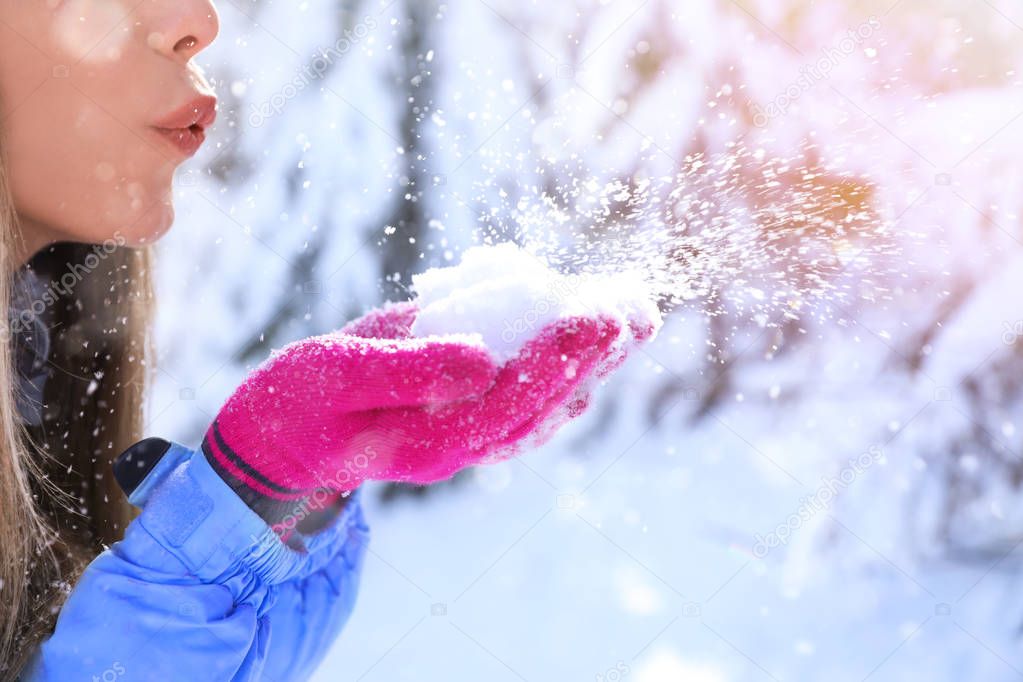 Woman blowing snow on sunny frosty day. Winter vacation