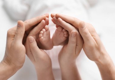 Young parents holding feet of their baby in hands clipart